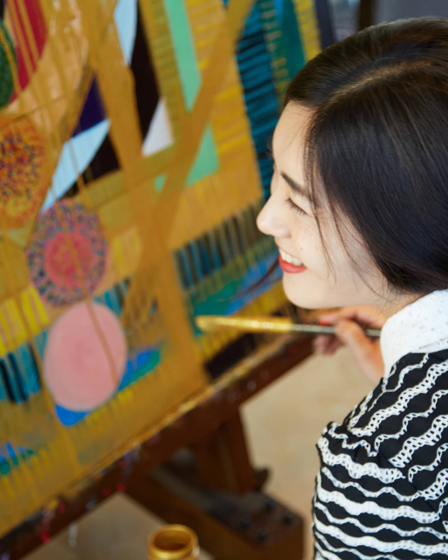 Side view of smiling woman's face as she holds paintbrush up to colourful painting