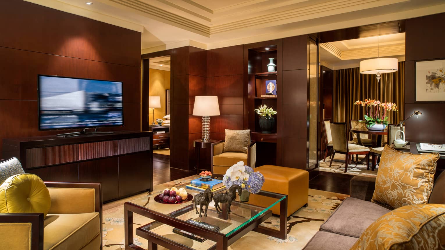 Beijing Suite living room with sofa, gold pillows and armchair, large TV, wood panel walls