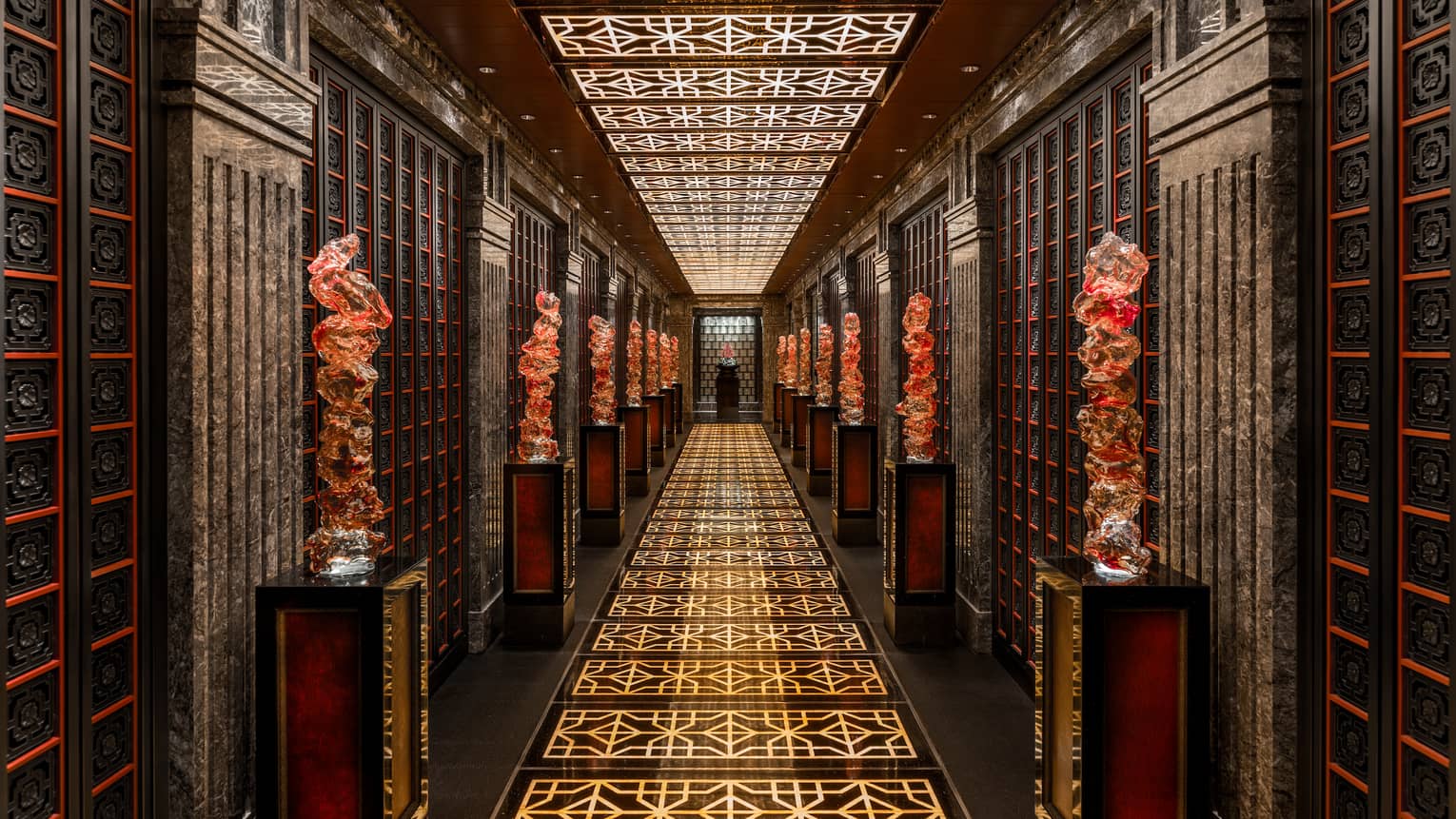 Long dimly-lit hallway at Cai Yi Xuan restaurant with gold pattern on floor, large red statues on pillars