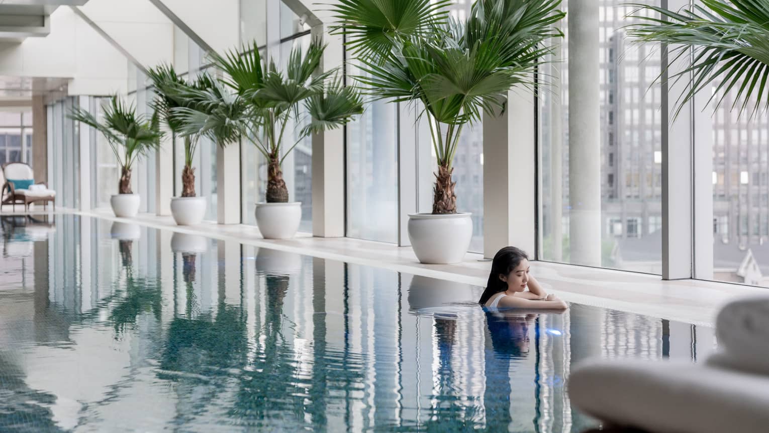 Female guest in sparkling pool surrounded by potted palms and floor-to-ceiling windows