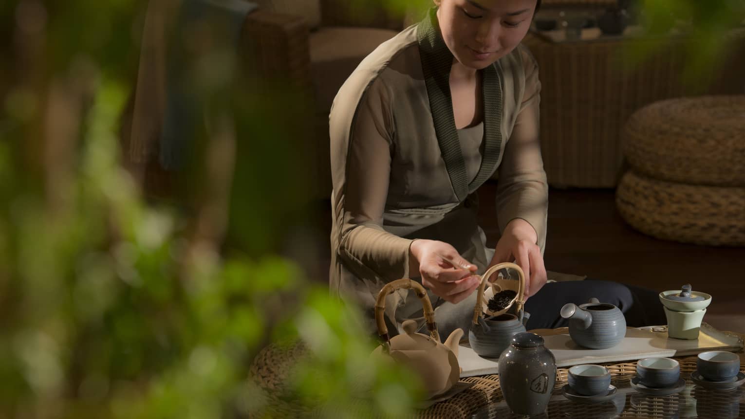 Woman spoons loose-leaf tea leaves into tea pots on tray