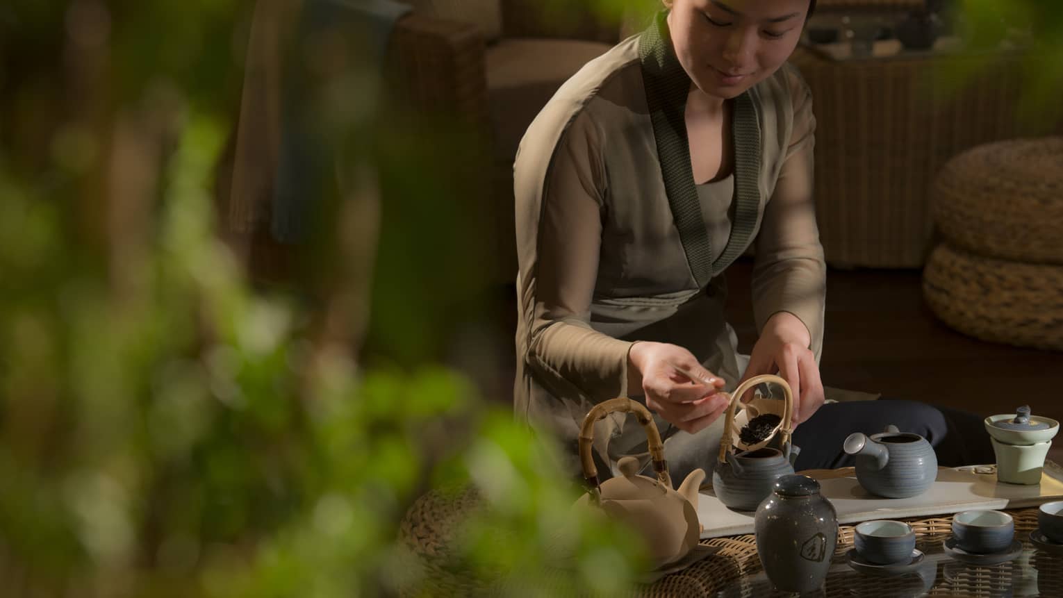 Woman spoons loose-leaf tea leaves into tea pots on tray