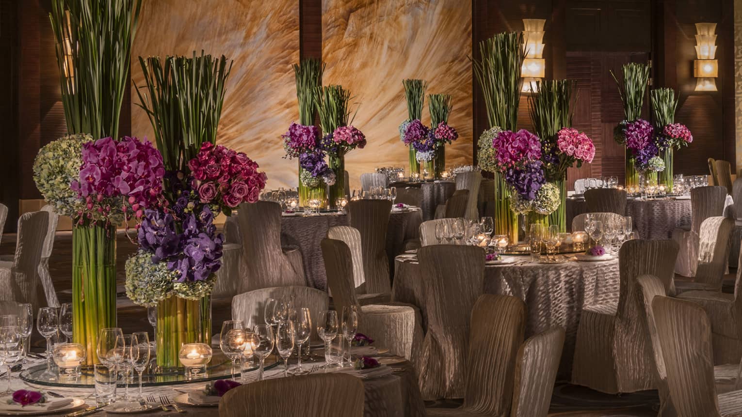 Elegant wedding reception, tables with large purple and green floral arrangements and glowing candles