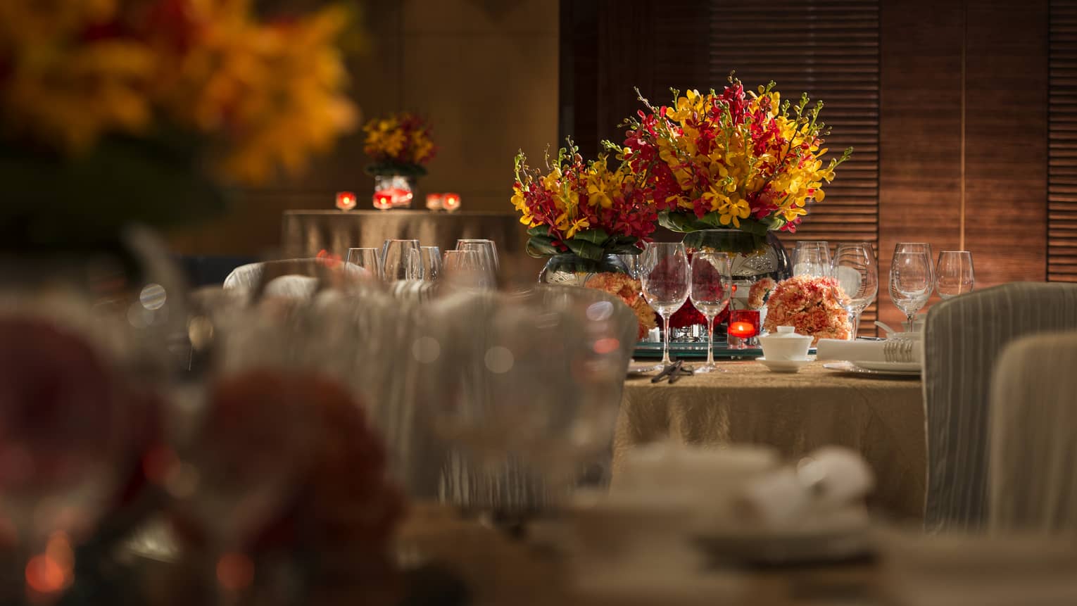 Orange and red flowers, candles on round banquet tables with gold linens