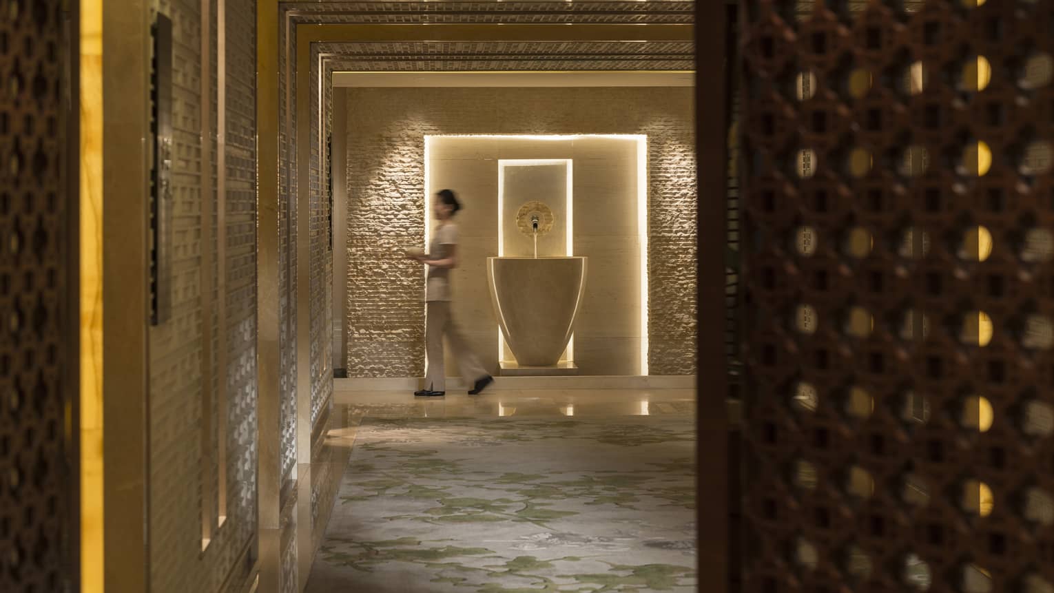 Spa staff walks with towels down marble hall past tall vase