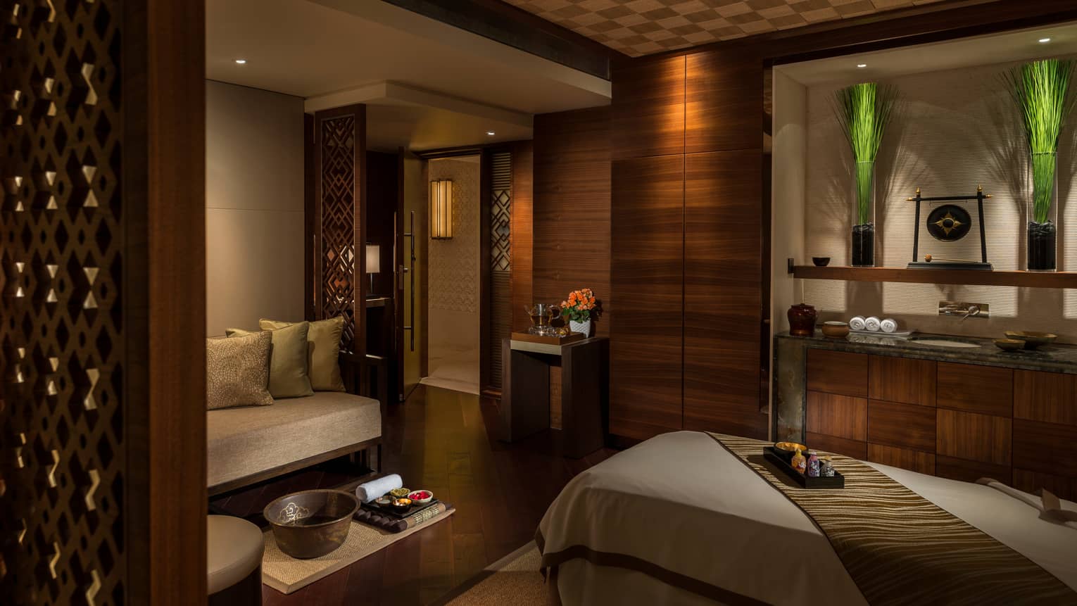 Spa treatment room with carved wood detail walls, bed and table with trays with oils