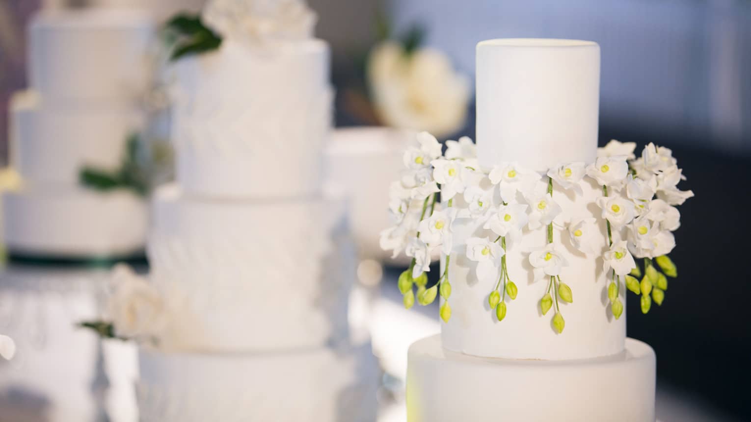 Three-tiered wedding cakes are each garnished with white florals 