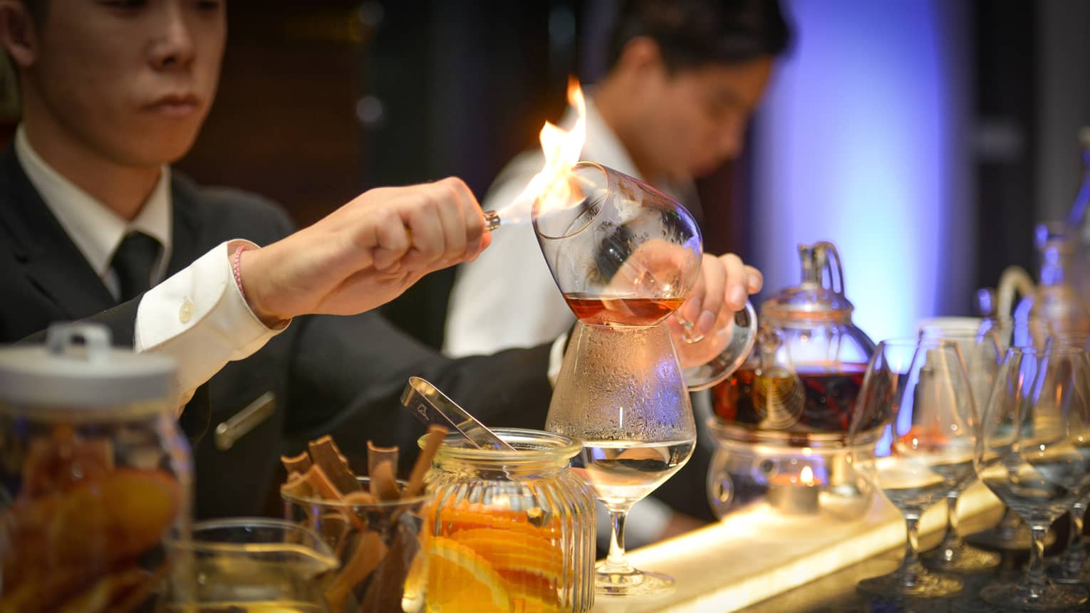 Opus Bar bartender holds flame to glass of liquor, prepares to pour it into cup