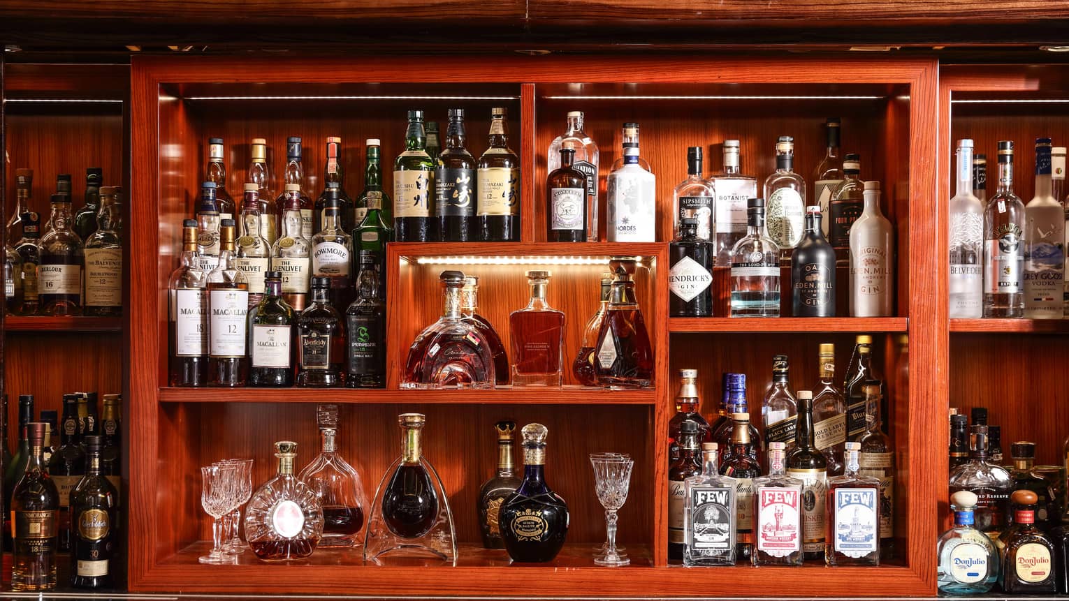 Wood back bar display lined with lights, with rows of liquor bottles