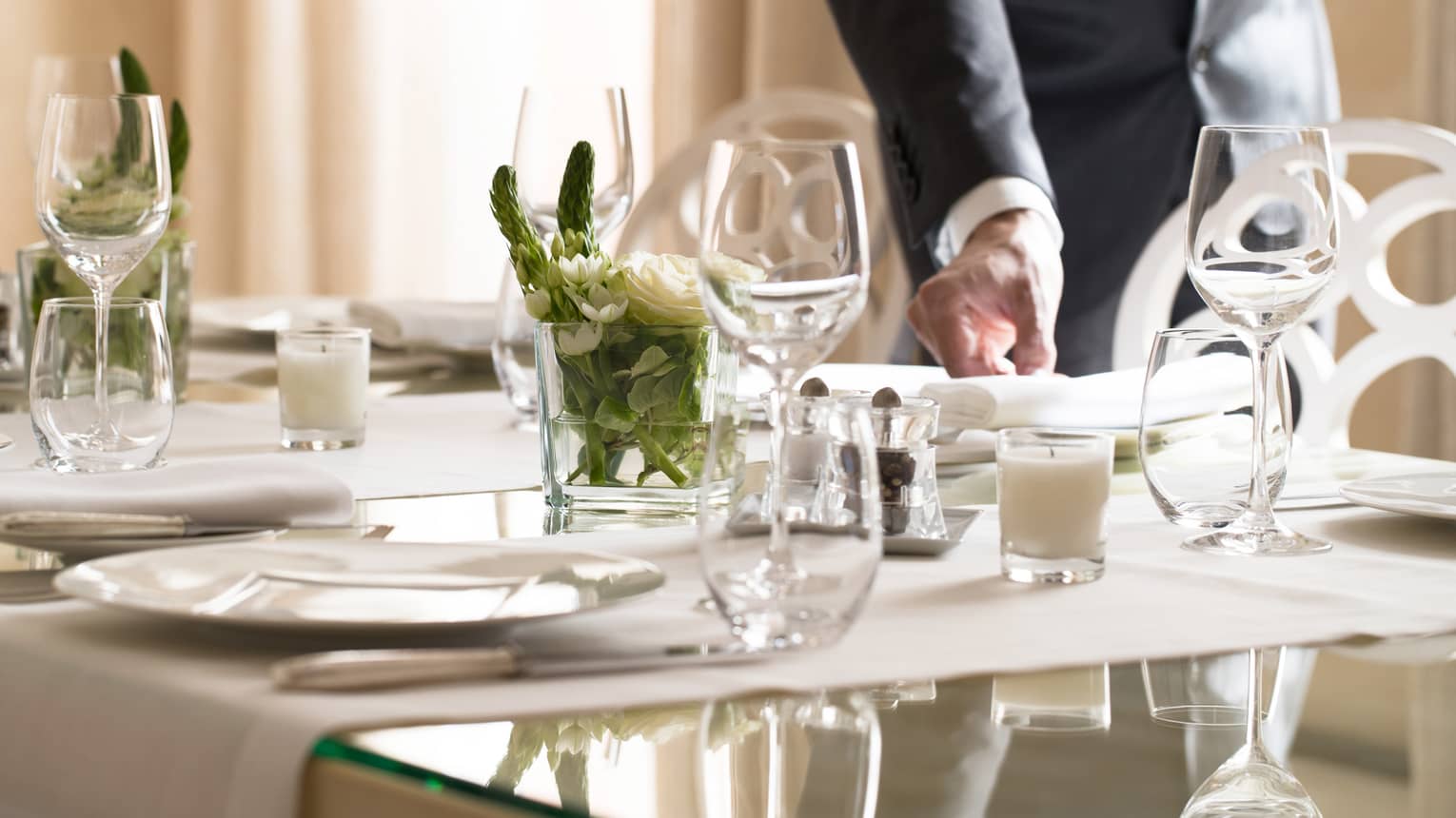 Hotel staff places napkin on small, elegant dining table in sunny room