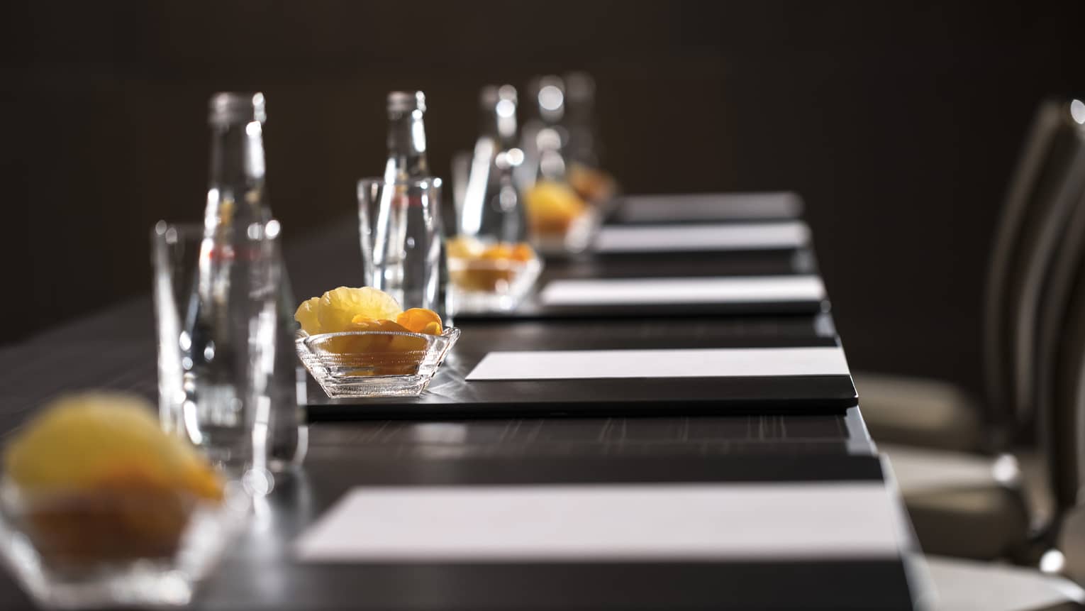 Row of glass bottles, small dishes with dried fruits, meeting agendas along boardroom table